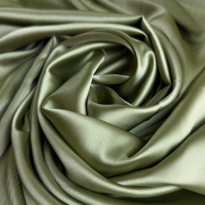 Może przedstawiać: Zbliżenie na miękką, zieloną satynową tkaninę udrapowaną w wirujący wzór. Tkanina jest gładka i luksusowa, z subtelnym połyskiem.