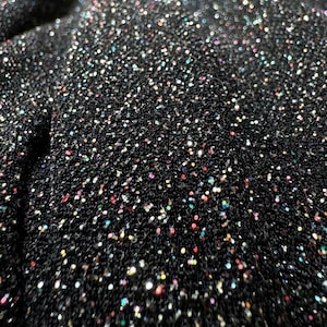 Pode incluir: Tecido preto com uma textura brilhante e iridescente. O tecido &eacute; coberto por pequenas lantejoulas coloridas.