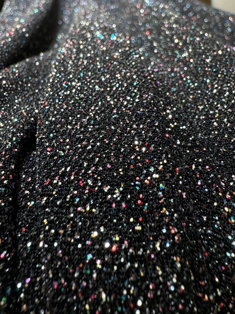 Pode incluir: Tecido preto com uma textura brilhante e iridescente. O tecido &eacute; coberto por pequenas lantejoulas coloridas.