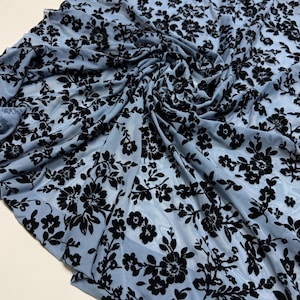 Könnte beinhalten: Blauer, durchsichtiger Stoff mit einem schwarzen Blumenmuster. Der Stoff ist weich und zart, und das Blumenmuster ist filigran und elegant.