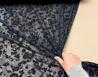 May include: Black floral patterned fabric with the word "BLACK" in a white font. The fabric is being held up to show the design. The text "COLORS MIGHT APPEAR SLIGHTLY DIFFERENT IN TINT WHEN VIEWED ONLINE COMPARED TO IN-PERSON" is also visible.