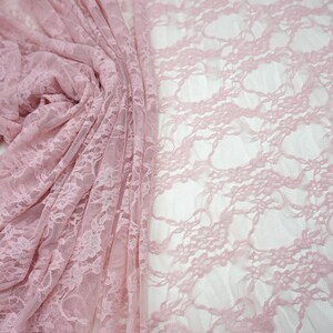 May include: A close-up of delicate, light pink lace fabric. The fabric is draped and folded, revealing intricate floral patterns. The lace has a soft, airy appearance, perfect for various craft projects or apparel.