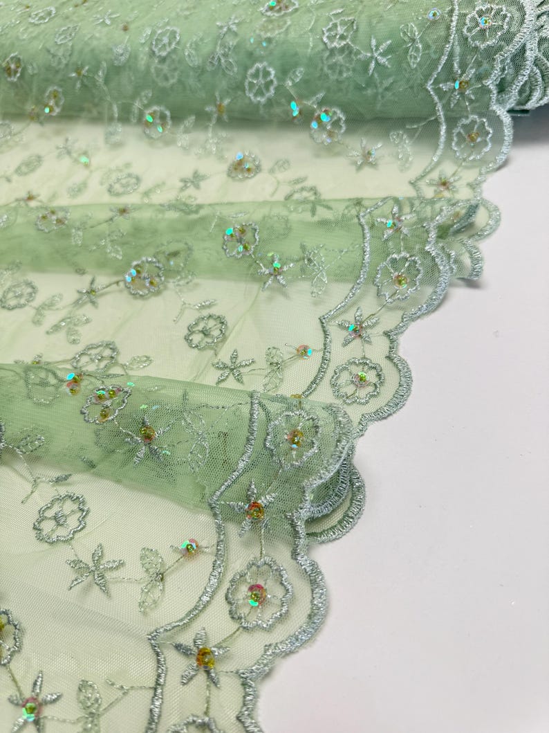 Peut inclure: Un rouleau de tissu en dentelle vert clair avec des motifs floraux et &eacute;toil&eacute;s brod&eacute;s. Le tissu pr&eacute;sente des paillettes iris&eacute;es et un bord festonn&eacute; avec du fil argent&eacute;. Le design d&eacute;licat convient &agrave; l'artisanat et aux v&ecirc;tements.
