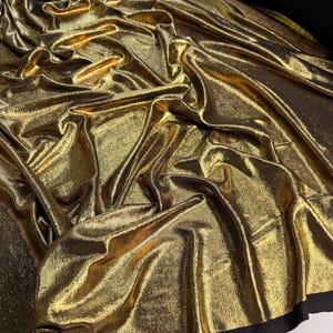 Könnte beinhalten: Goldfarbener Metallic-Stoff mit einer strukturierten Oberfläche. Der Stoff ist zerknittert und hat einen leichten Glanz.