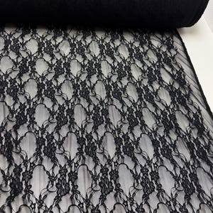 K&ouml;nnte beinhalten: Eine Rolle schwarzer Webspitze mit floralem Muster. Der Stoff ist 137/152 cm breit und besteht aus 90 % Nylon und 10 % Elasthan. Die Spitze hat ein zartes, offenes Webdesign.