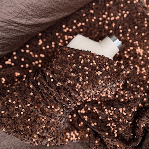Puede incluir: Tela de terciopelo marrón con estiramiento bidireccional, cubierta de pequeñas lentejuelas de cobre brillantes.  "Brown velvet 2-way stretch for evening gowns" está escrito en la parte inferior de la imagen.