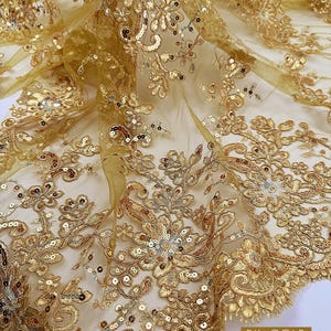 May include: DK. GOLD lace fabric with intricate floral embroidery and sequins. The fabric is a rich gold color and is 53/54 inches wide. The text on the image says "Multiple yards will come in one continuous piece."