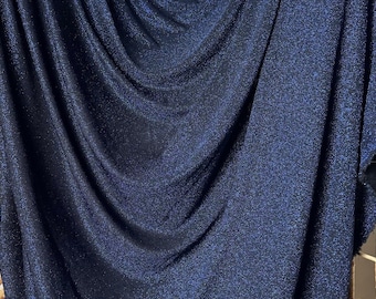 Könnte beinhalten: Nahaufnahme eines dunkelblauen Stoffes mit glitzernder Textur. Der Stoff ist drapiert und gefaltet und zeigt seine weiche und fließende Beschaffenheit.