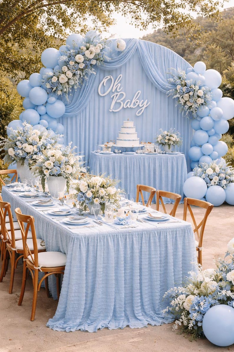 Op de afbeelding: Een babyborrel ingericht in lichtblauw. De sc&egrave;ne toont een tafelsetting met bloemstukken, een taart en een achtergrond met ballonnen en de tekst "Oh Baby". Houten stoelen en een lange tafel zijn gedekt voor de gasten.