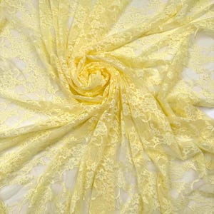 K&ouml;nnte beinhalten: Nahaufnahme eines zarten, hellgelben Spitzenstoffs. Der Stoff ist mit aufwendigen floralen Mustern versehen und in weichen Falten drapiert, wodurch ein Gef&uuml;hl von Tiefe und Textur entsteht. Die Spitze ist halbtransparent und l&auml;sst den Hintergrund durchscheinen.