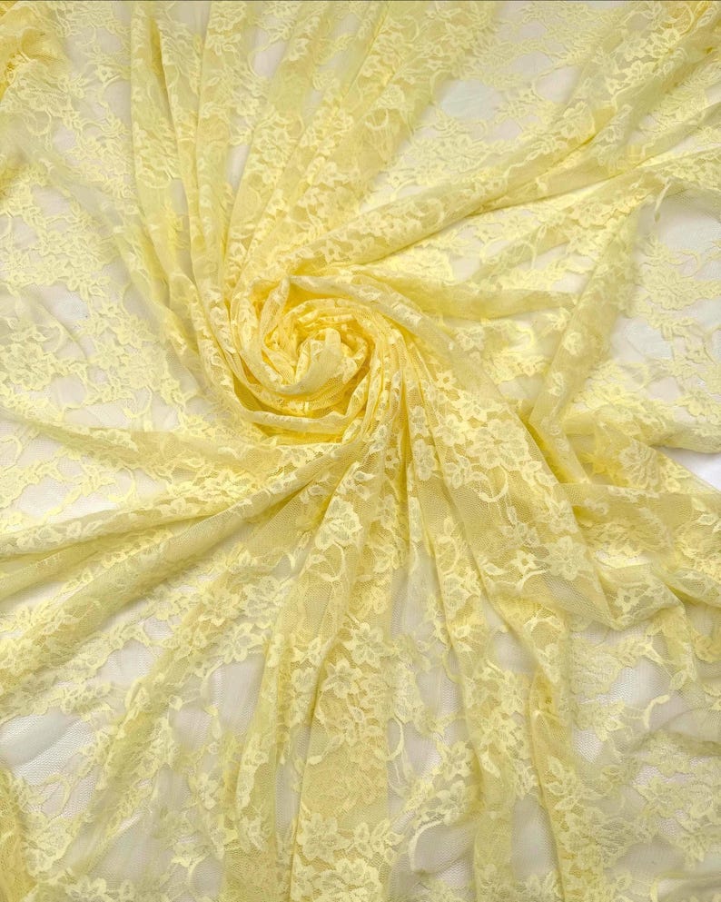 K&ouml;nnte beinhalten: Nahaufnahme eines zarten, hellgelben Spitzenstoffs. Der Stoff ist mit aufwendigen floralen Mustern versehen und in weichen Falten drapiert, wodurch ein Gef&uuml;hl von Tiefe und Textur entsteht. Die Spitze ist halbtransparent und l&auml;sst den Hintergrund durchscheinen.