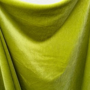 以下が含まれることがあります： 光沢のある、滑らかで柔らかな緑色のベルベット生地。生地はドレープされ、折り畳まれており、その質感とドレープが際立っています。