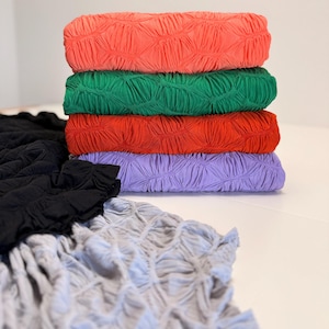 Könnte beinhalten: Ein Stapel von fünf Stoffproben in verschiedenen Farben, darunter Koralle, Grün, Rot, Lavendel und Grau. Der Stoff hat eine strukturierte, geknitterte Oberfläche.