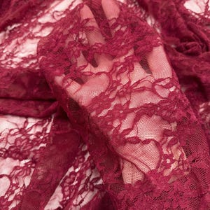 K&ouml;nnte beinhalten: Nahaufnahme von bordeauxfarbenem Spitzenstoff. Der zarte Stoff weist ein kompliziertes Blumenmuster auf. Das transparente Material ist drapiert und zeigt die Textur und das Design der Spitze. Die Farbe ist ein tiefer, satter Rotton.