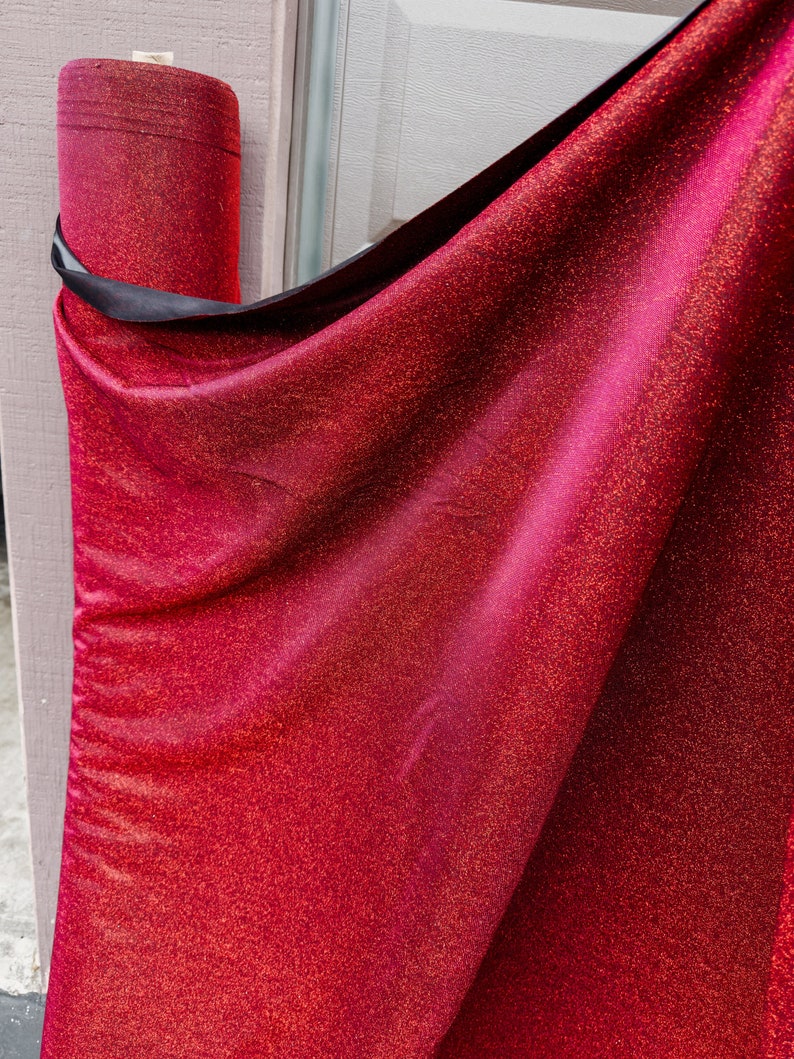 May include: A roll of red fabric with gold glitter. The fabric is rolled up and tied with a black ribbon.