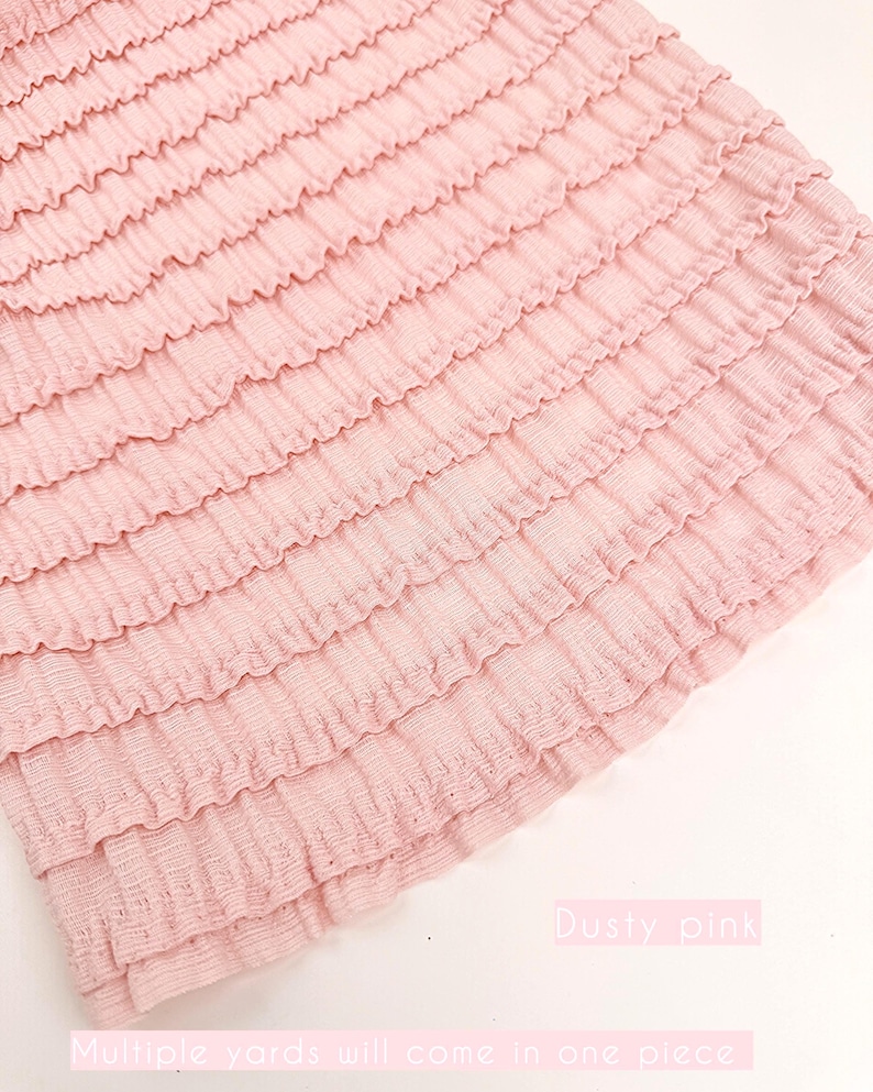 Op de afbeelding: Stof in stoffig roze met gelaagde ruches. De stof heeft een getextureerde uitstraling en is lichtroze van kleur. De tekst "Dusty pink" en "Multiple yards will come in one piece" zijn zichtbaar.