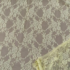 K&ouml;nnte beinhalten: Nahaufnahme eines hellgelben Spitzenstoffs. Die Spitze weist ein Blumenmuster mit zarten, miteinander verbundenen Designs auf. Der Stoff hat ein weiches, luftiges Aussehen mit einer leicht transparenten Qualit&auml;t. Die Kanten des Stoffes sind sichtbar und zeigen die Textur und die Details.