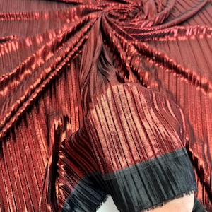 Puede incluir: Tela plisada metálica burdeos con ribete negro. La tela tiene un brillo sutil y es perfecta para crear prendas o accesorios.