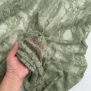 Pode incluir: Tecido de renda verde s&aacute;lvia com um delicado padr&atilde;o floral. O tecido &eacute; transparente e drapeado, com detalhes intrincados vis&iacute;veis em toda parte. A renda &eacute; macia e flex&iacute;vel, ideal para v&aacute;rios projetos de artesanato ou vestu&aacute;rio.