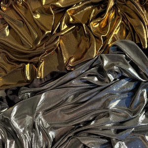 May include: A collection of metallic fabric featuring two distinct sections. The top portion is a shimmering gold material with deep folds and creases. The bottom portion is a reflective silver fabric with a similar draped, textured appearance.