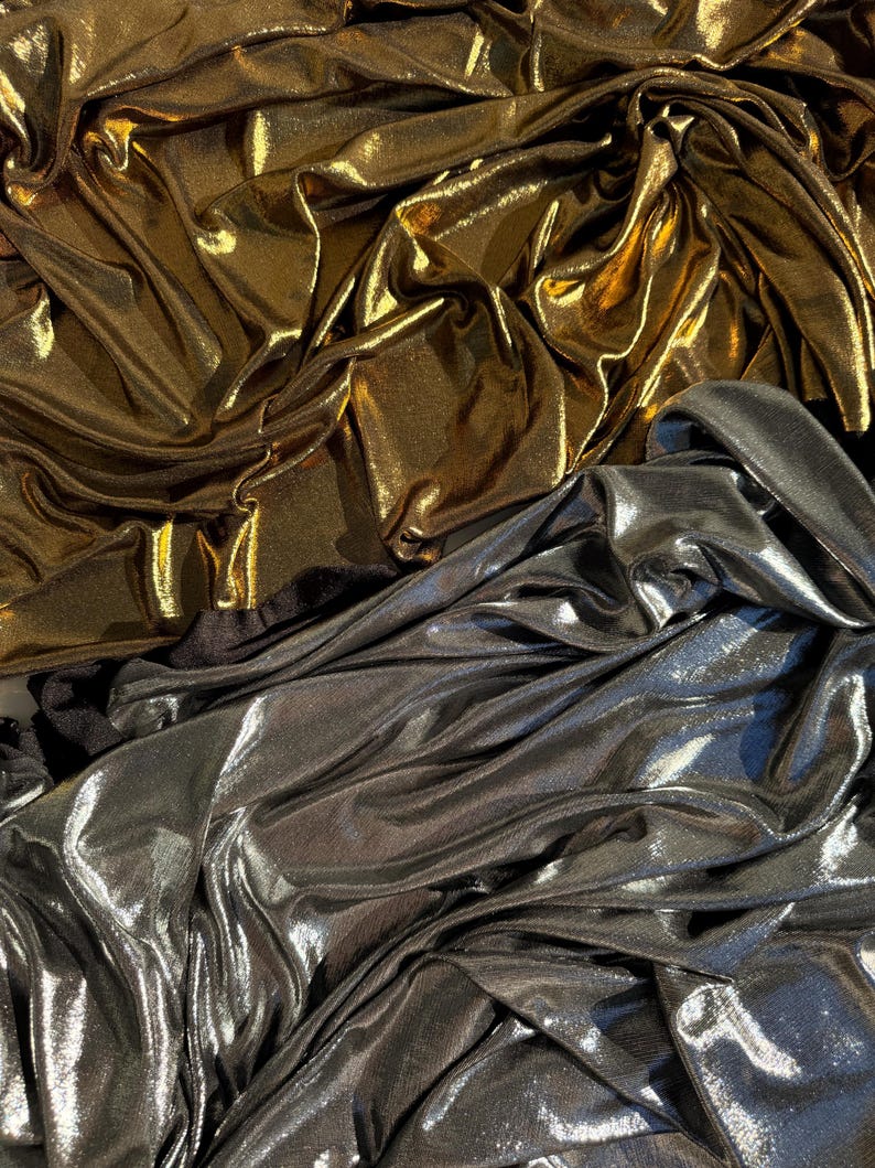 May include: A collection of metallic fabric featuring two distinct sections. The top portion is a shimmering gold material with deep folds and creases. The bottom portion is a reflective silver fabric with a similar draped, textured appearance.
