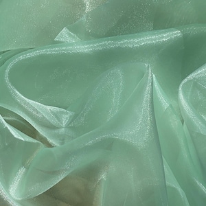 May include: A piece of light green sheer fabric with a shimmery finish. The fabric is folded and draped, showing its texture and drape.