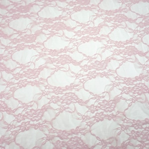May include: Close-up of a light pink lace fabric. The delicate lace features a floral pattern with a repeating design. The fabric is semi-transparent, with a soft, textured appearance. The background is white.