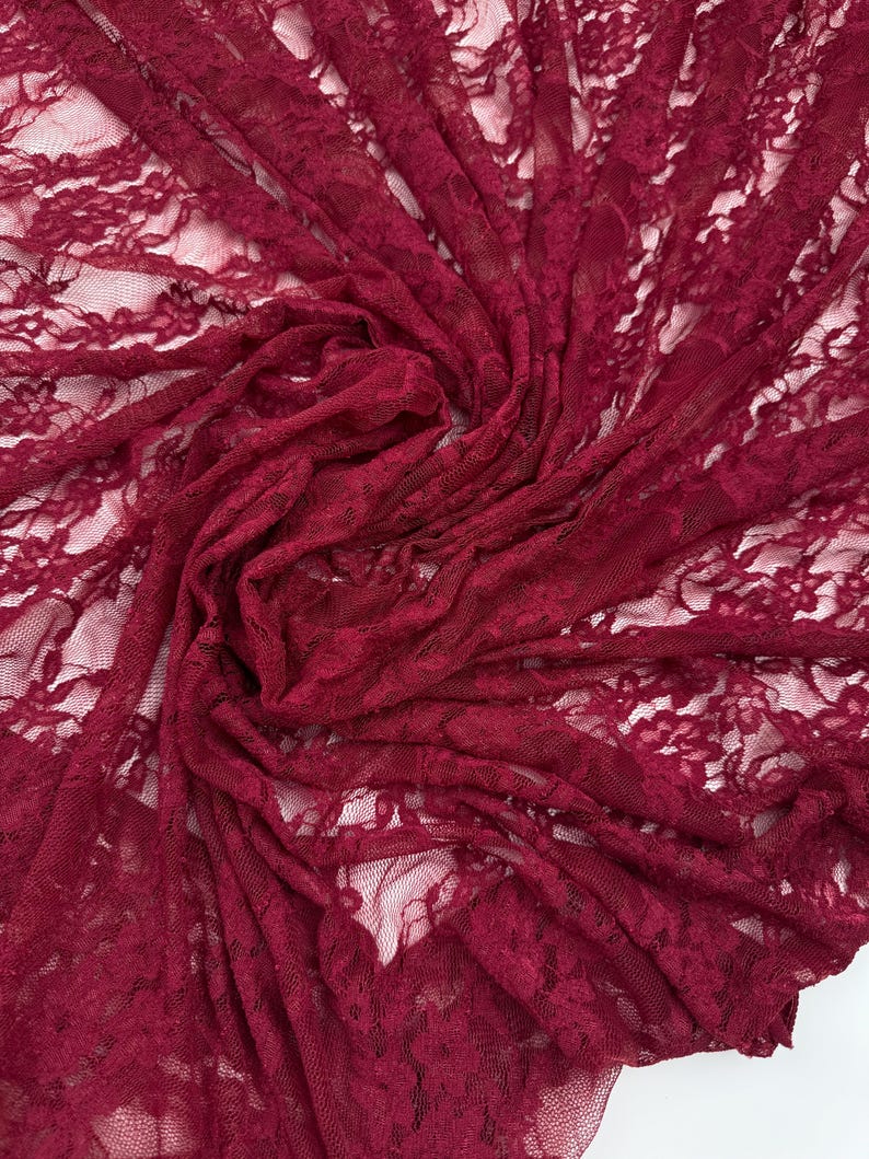 K&ouml;nnte beinhalten: Nahaufnahme eines tiefroten Spitzenstoffs. Das zarte Blumenmuster ist im gesamten Textil sichtbar. Der Stoff ist gerafft und drapiert, wodurch Schatten entstehen und die komplizierten Details der Spitze hervorgehoben werden. Ideal f&uuml;r Kleidung und Bastelprojekte.