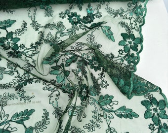 May include: Green floral lace fabric with sequins. The lace has a delicate floral pattern with small green sequins throughout. The fabric is sheer and has a soft, flowing texture.