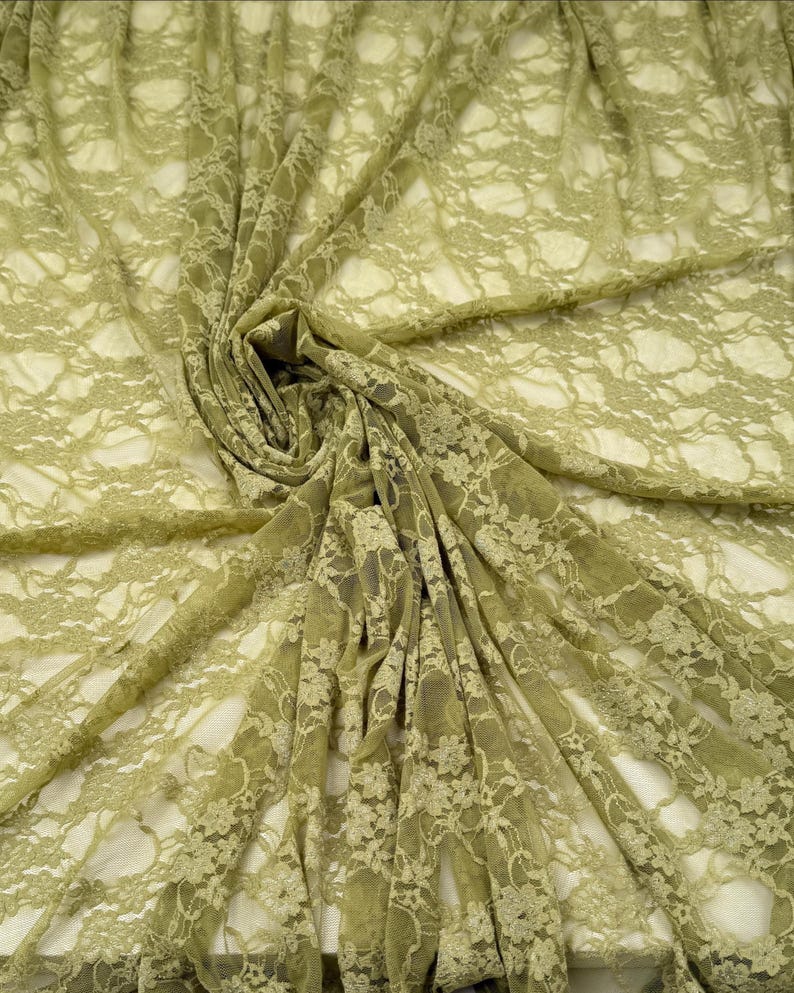 May include: Olive green lace fabric with a floral pattern. The fabric is draped and folded, creating shadows and depth. The lace has a delicate, open weave, and the color is a muted, earthy tone. This fabric is suitable for apparel and craft projects.
