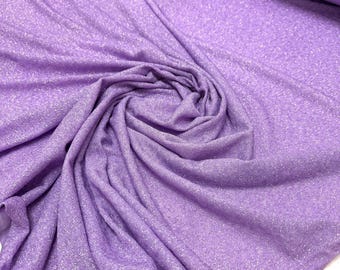 May include: A bolt of lavender fabric with a subtle shimmering finish. The material is draped in soft, flowing folds, revealing a fine, glittery texture across the surface. The light purple textile has a consistent, woven appearance throughout.