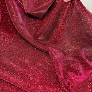 May include: Red sparkly fabric with a shimmery finish. The fabric has a fine, textured weave and a subtle sheen.