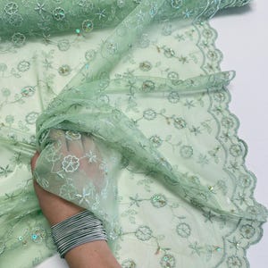 Peut inclure: Tissu en dentelle vert clair avec des fleurs brod&eacute;es et des paillettes. Le tissu d&eacute;licat est pli&eacute;, r&eacute;v&eacute;lant les d&eacute;tails complexes du motif. La dentelle a un bord festonn&eacute;. Id&eacute;al pour la couture.