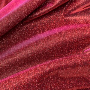 May include: Red sparkly fabric with a subtle pink sheen. The fabric has a fine, woven texture and a shimmery finish.