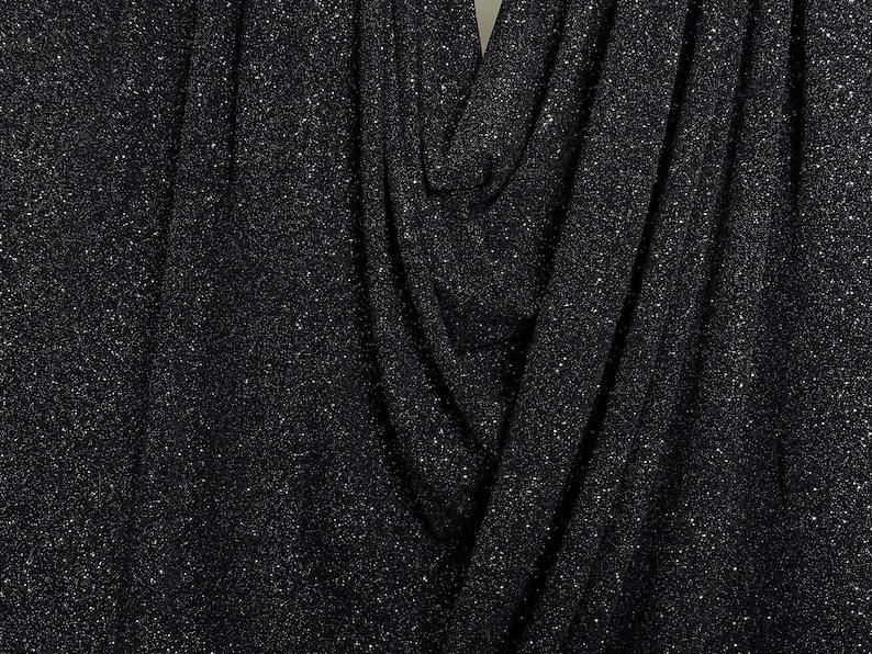 Pode incluir: Tecido preto com acabamento texturizado brilhante. O tecido &eacute; drapeado e dobrado, criando um visual suave e fluido.