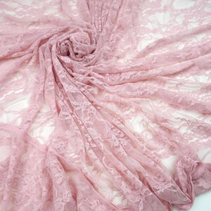 May include: A close-up shot of a delicate, light pink lace fabric. The fabric is draped and swirled, creating a soft, textured appearance. The lace features a floral pattern, adding to its romantic and feminine aesthetic. Ideal for bridal wear or craft projects.