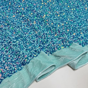 Può includere: Un tessuto blu turchese con paillettes iridescenti. Il tessuto ha una texture morbida e vellutata.
