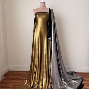May include: A floor-length strapless gown featuring a metallic gold fabric bodice and skirt, accented by a long, flowing metallic silver train attached to the side. The garment includes black trim along the neckline and the edges of the silver fabric.