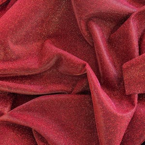 May include: Red sparkly fabric with a shimmery finish. The fabric is wrinkled and folded.