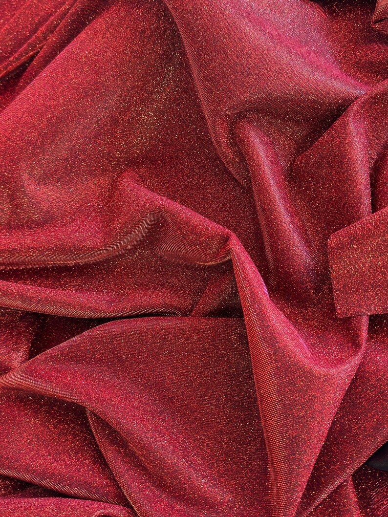 May include: Red sparkly fabric with a shimmery finish. The fabric is wrinkled and folded.