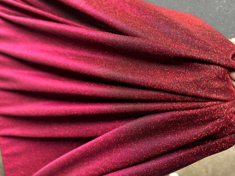 May include: Close-up of a burgundy fabric with a subtle shimmer. The fabric has a fine, textured weave and a soft, drapey feel.