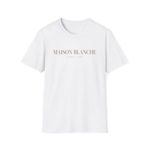 May include: A white short-sleeved t-shirt featuring the text MAISON BLANCHE in a brown serif font across the chest, with the smaller text SINCE 1987 printed directly underneath in a matching brown color, centered on the front of the garment.