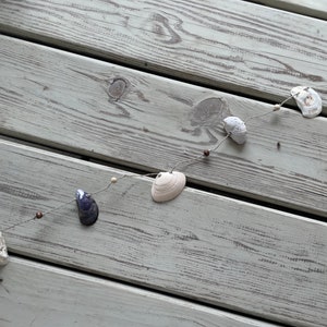 以下が含まれることがあります： 白と紫の貝殻が茶色のビーズで紐に通された貝殻のガーランド
