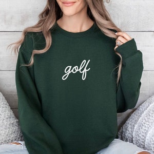 Puede incluir: Una sudadera verde oscuro con la palabra "golf" escrita en cursiva blanca en la parte delantera.