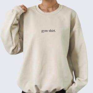 simple beige gym sweatshirt featuring a minimalist text design. Made with the Gildan 18000 sweatshirt