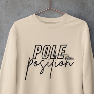 Puede incluir: Una sudadera beige con el texto "POLE position" en negro, con un gráfico de coche de carreras estilizado.