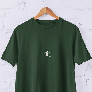 Könnte beinhalten: Ein dunkelgrünes T-Shirt mit einer weißen Grafik eines Skifahrers auf der Vorderseite.
