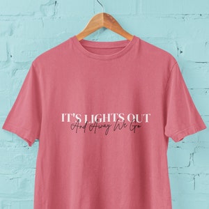Puede incluir: Una camiseta rosa con el texto "It's Lights Out And Away We Go" impreso en la parte delantera en blanco.