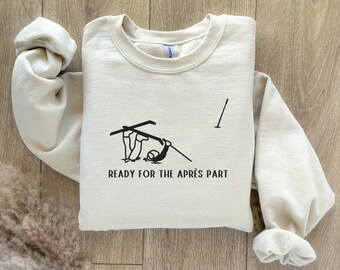 Puede incluir: Una sudadera beige con un gráfico negro de un esquiador cayendo con el texto "READY FOR THE APRÈS PART" impreso en la parte delantera.