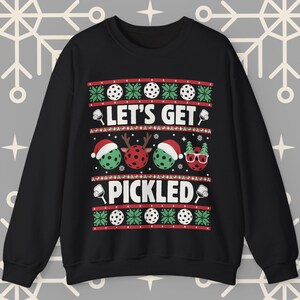 Peut inclure: Pullover de Noël noir sur le thème du pickleball. Il présente un motif vert et blanc avec le texte "Let's Get Pickled".